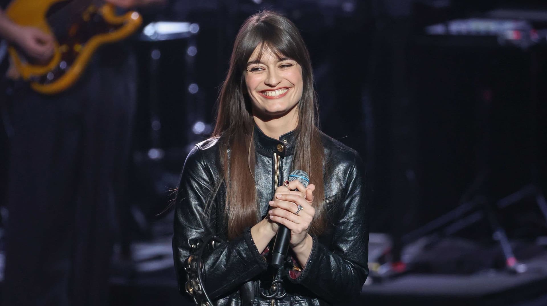 Clara Luciani souriante, veste en cuir noir, micro à la main