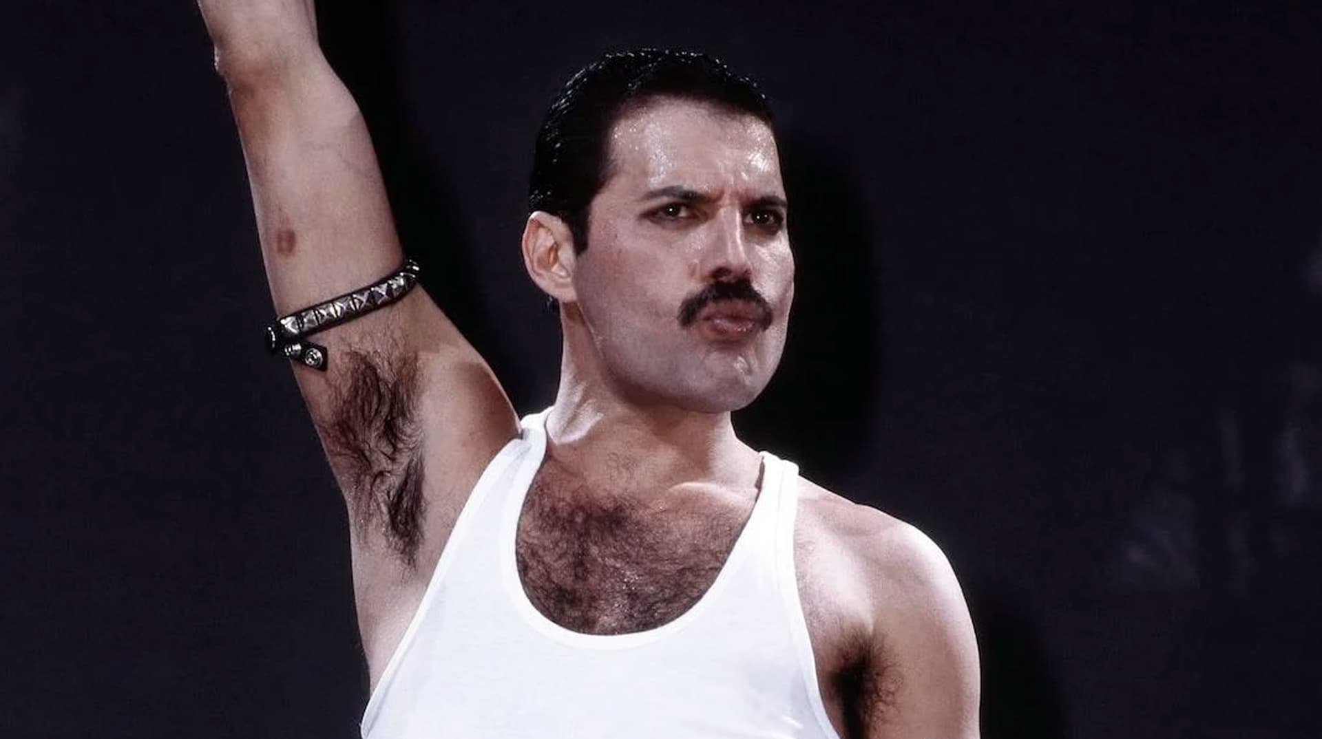 Freddie Mercury en débardeur blanc, bras levé, sur scène