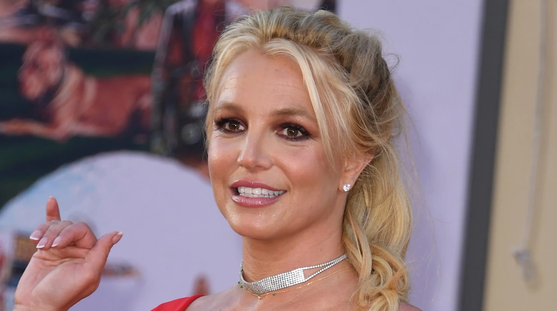 Britney Spears souriante, cheveux blonds, fait un signe de la main