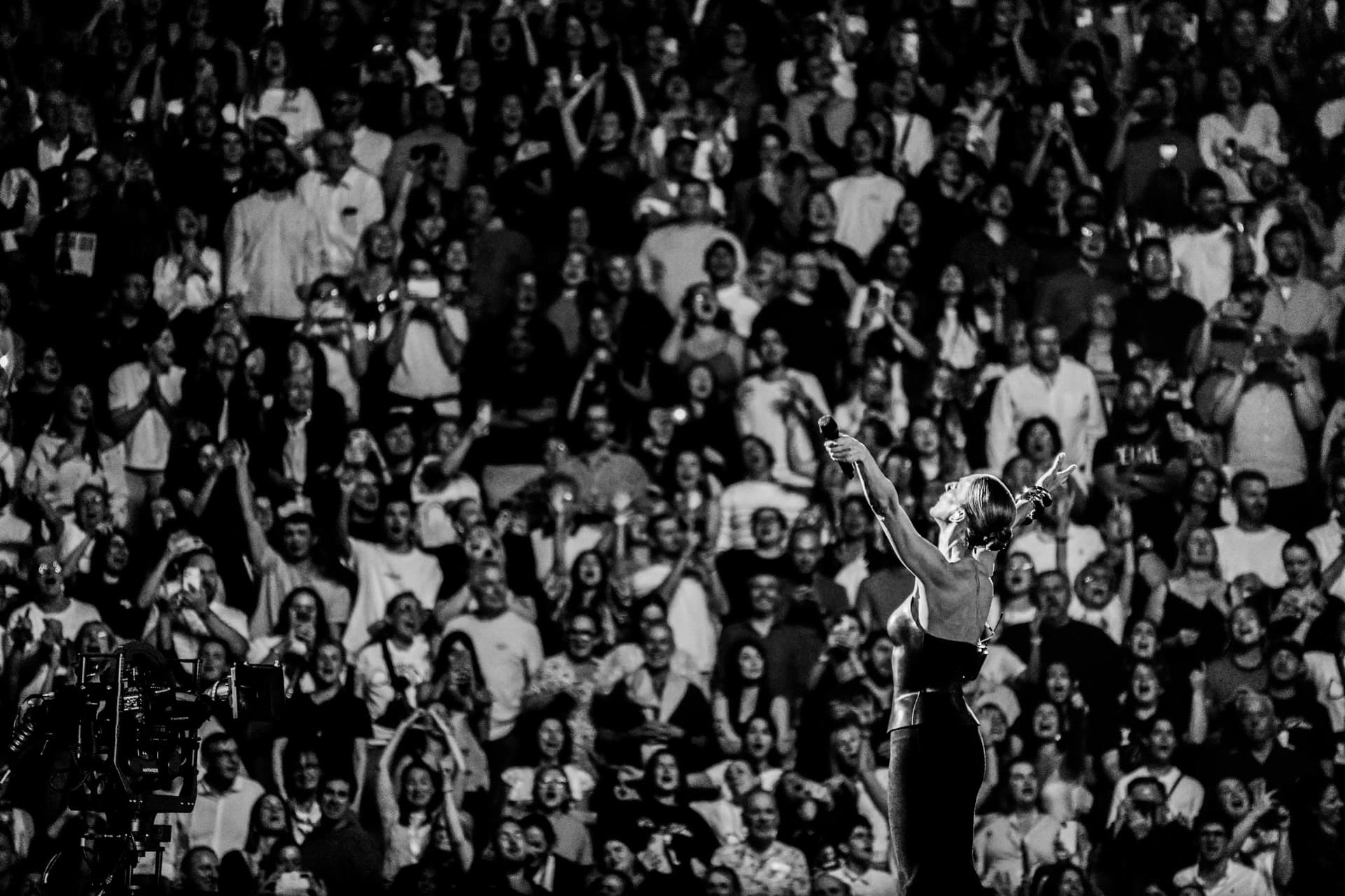 Photo en noir et blanc : Céline Dion sur scène tend les bras vers une salle comble