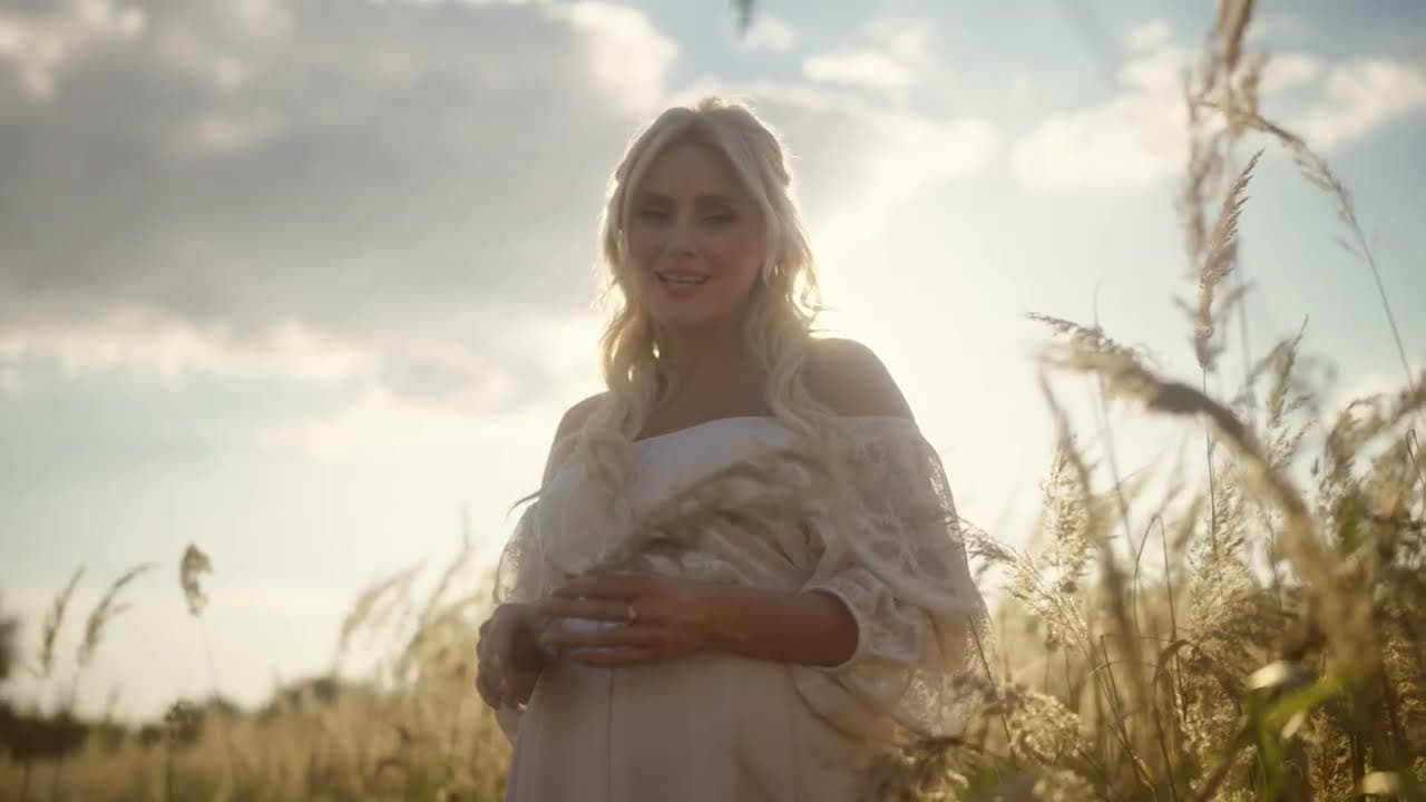 Iryna Fedyshyn en robe claire, debout dans les hautes herbes sous un ciel nuageux