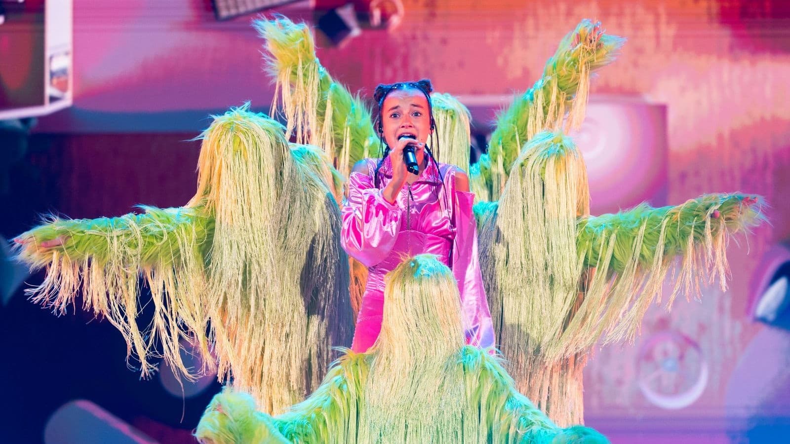 Erika Kolesnichenko en costume rose chante entourée de danseurs en costumes verts à franges