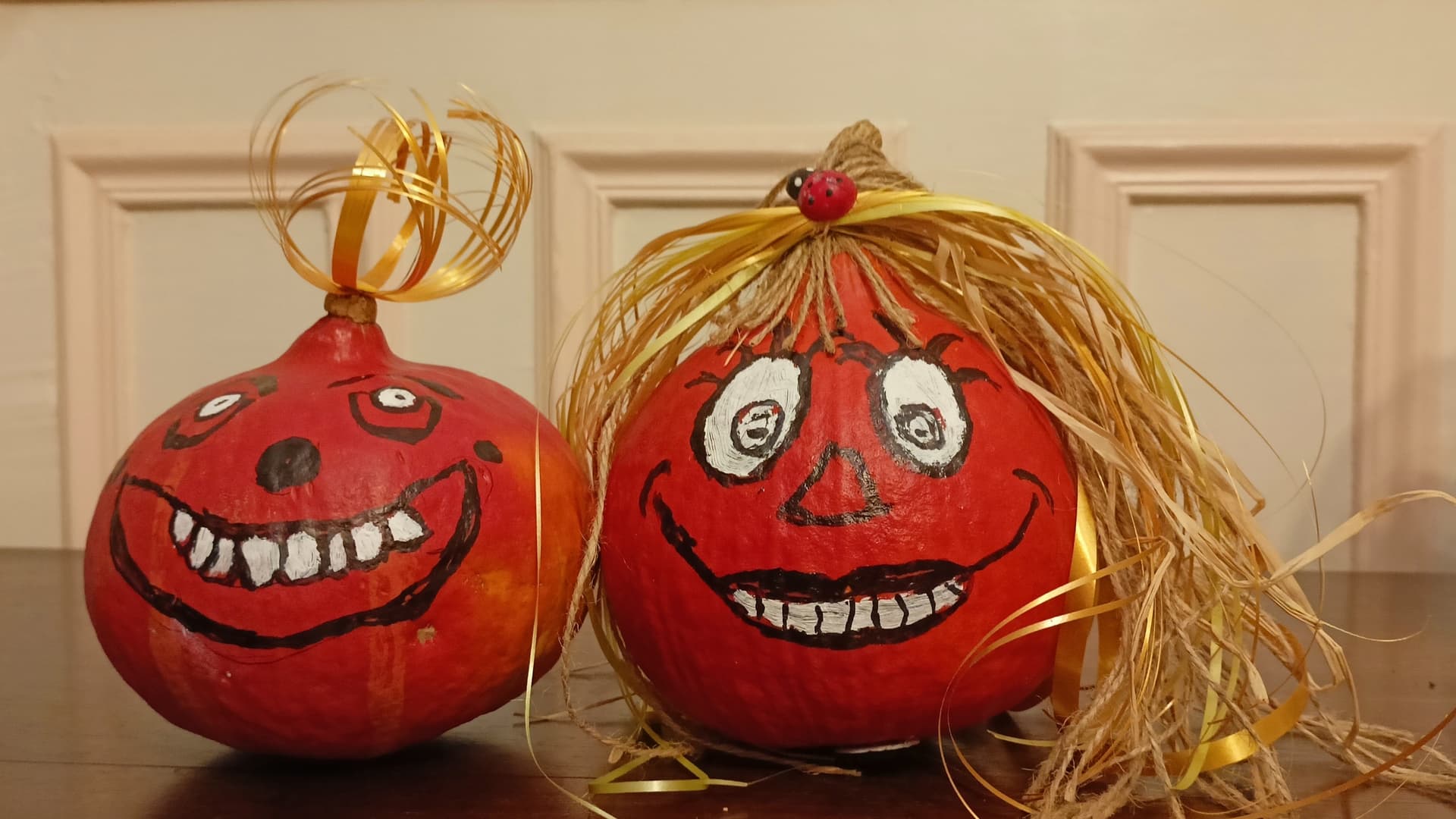 Deux potimarrons rouges peints de visages souriants, avec des cheveux en raphia