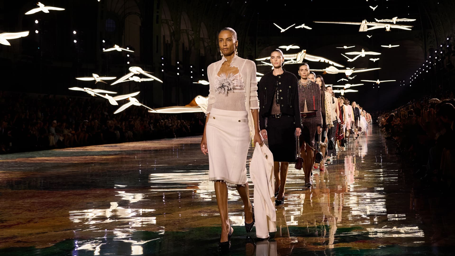 Mannequins Chanel défilant au Grand Palais sous des oiseaux lumineux, reflétés par le sol
