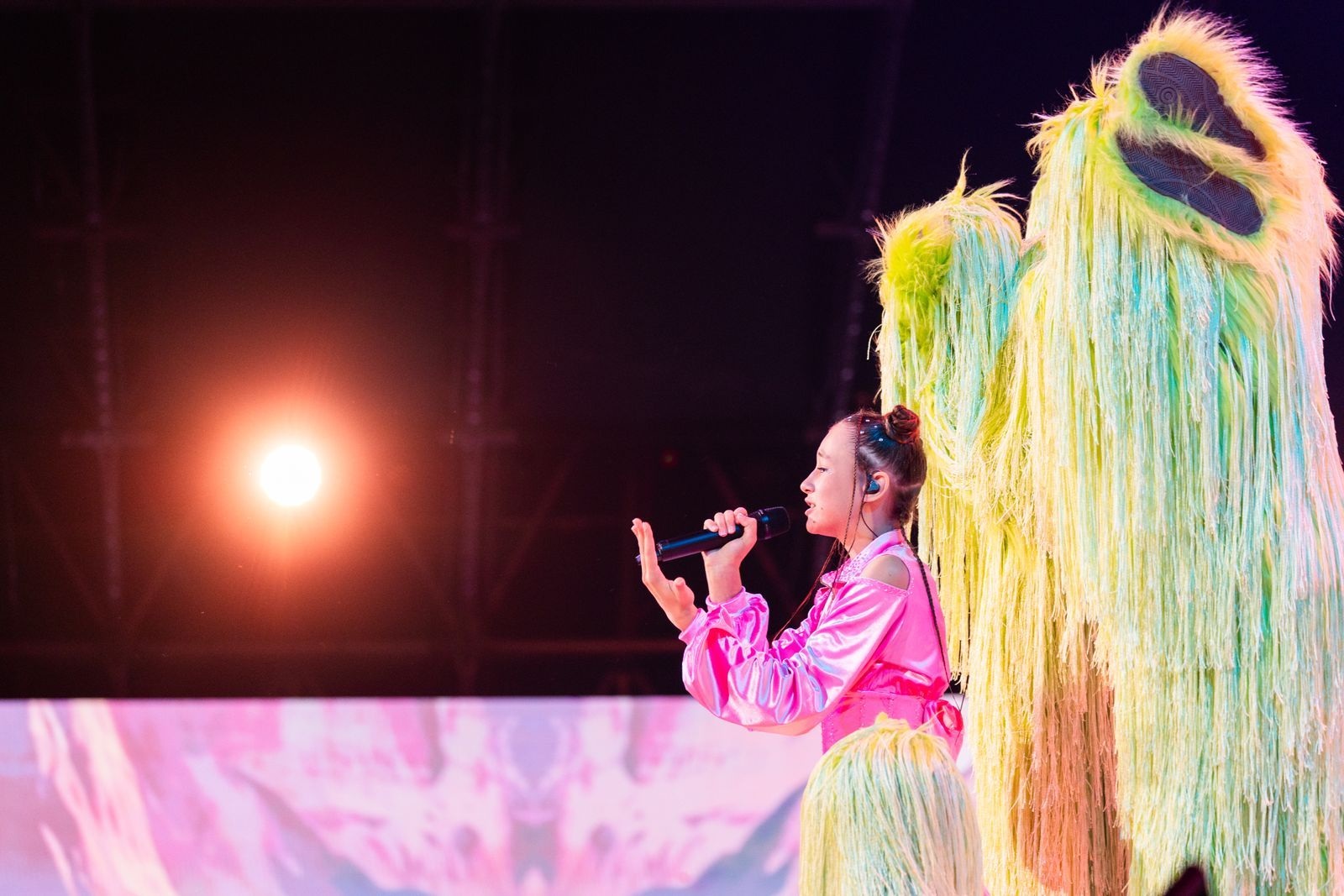 Erika Kolesnichenko en costume rose chante de profil à côté d’un danseur en costume vert à franges