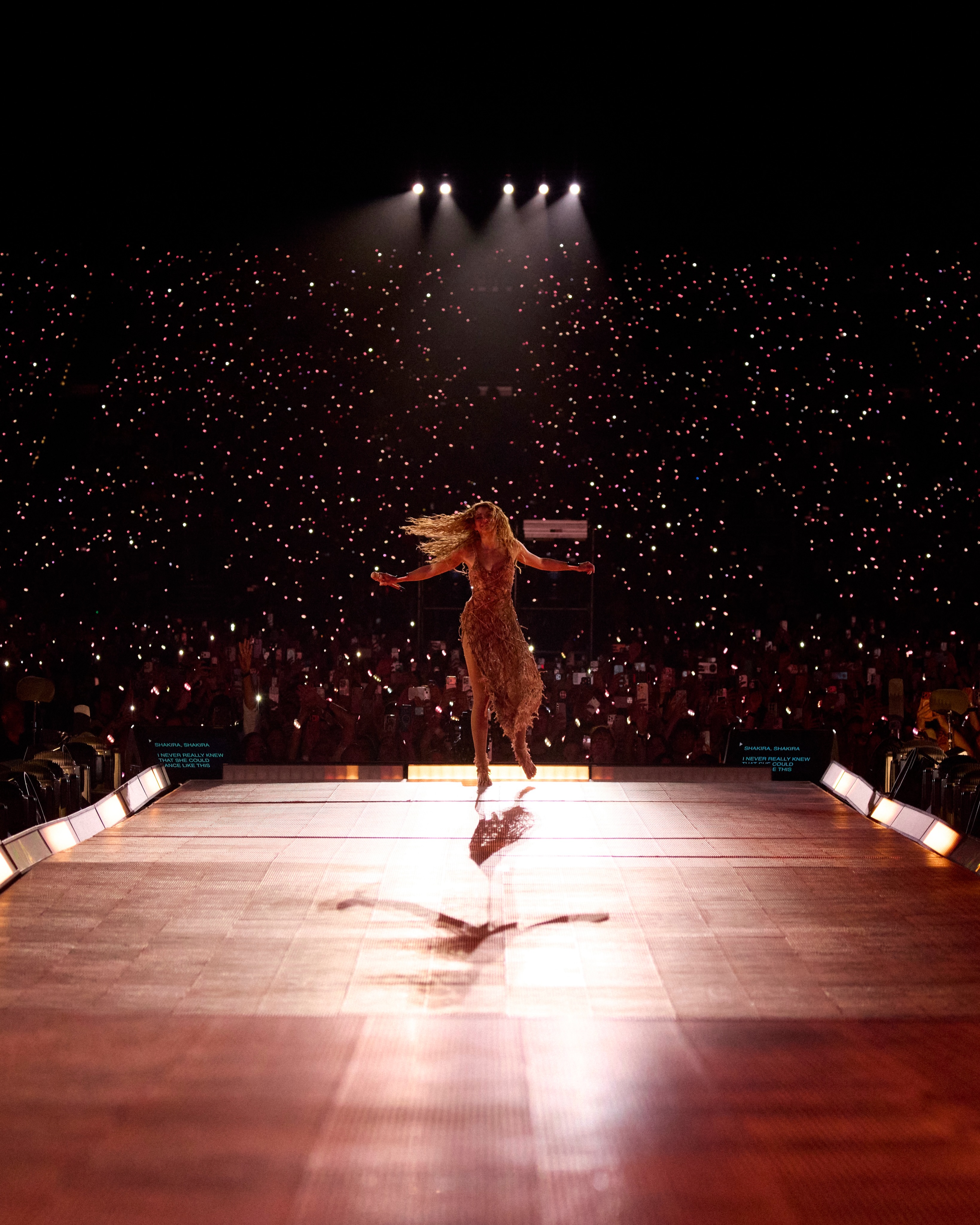 Shakira sur une avancée de scène au milieu du stade, bras écartés, face à des milliers de lumières