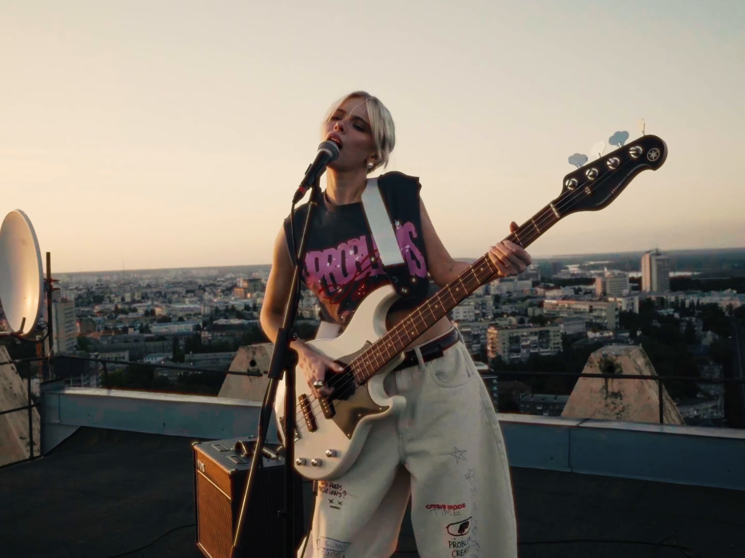 Masha Kondratenko chante avec une basse blanche sur un toit, avec le panorama de Kyiv derrière elle