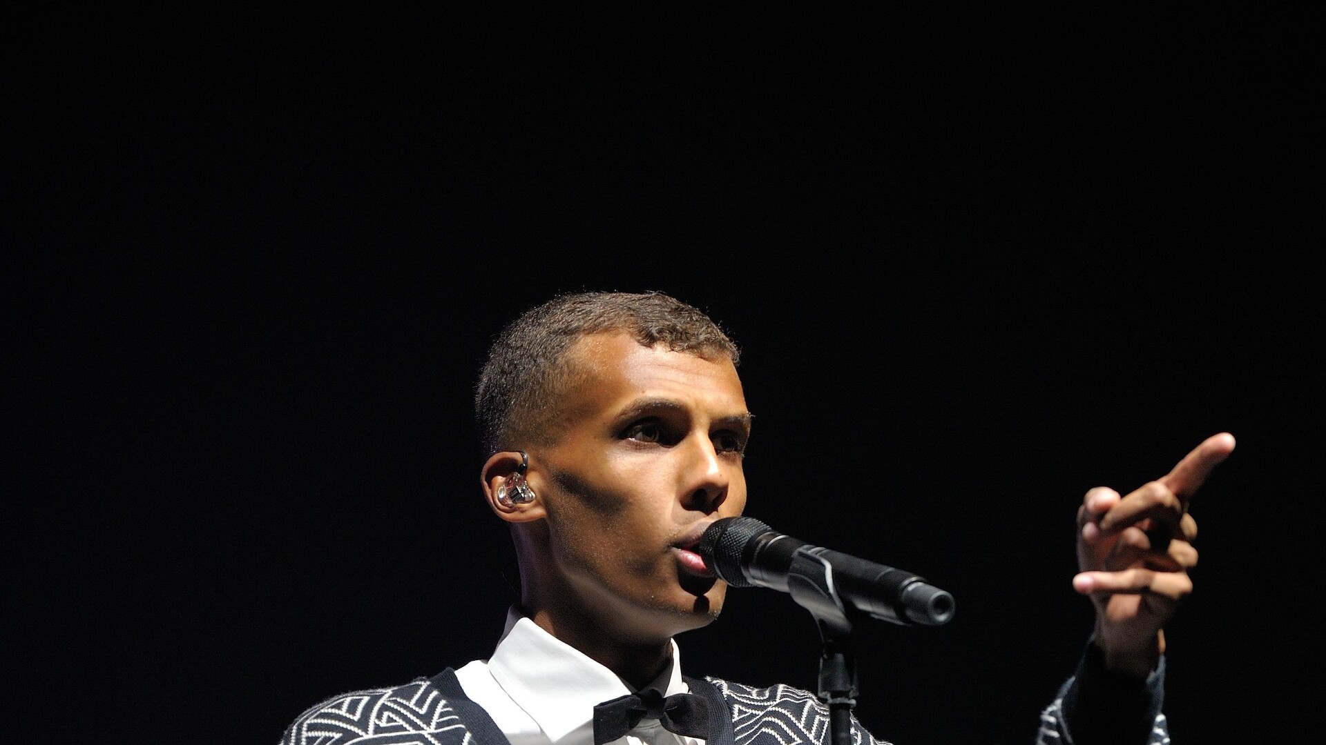 Stromae співає в мікрофон на сцені, чорне тло