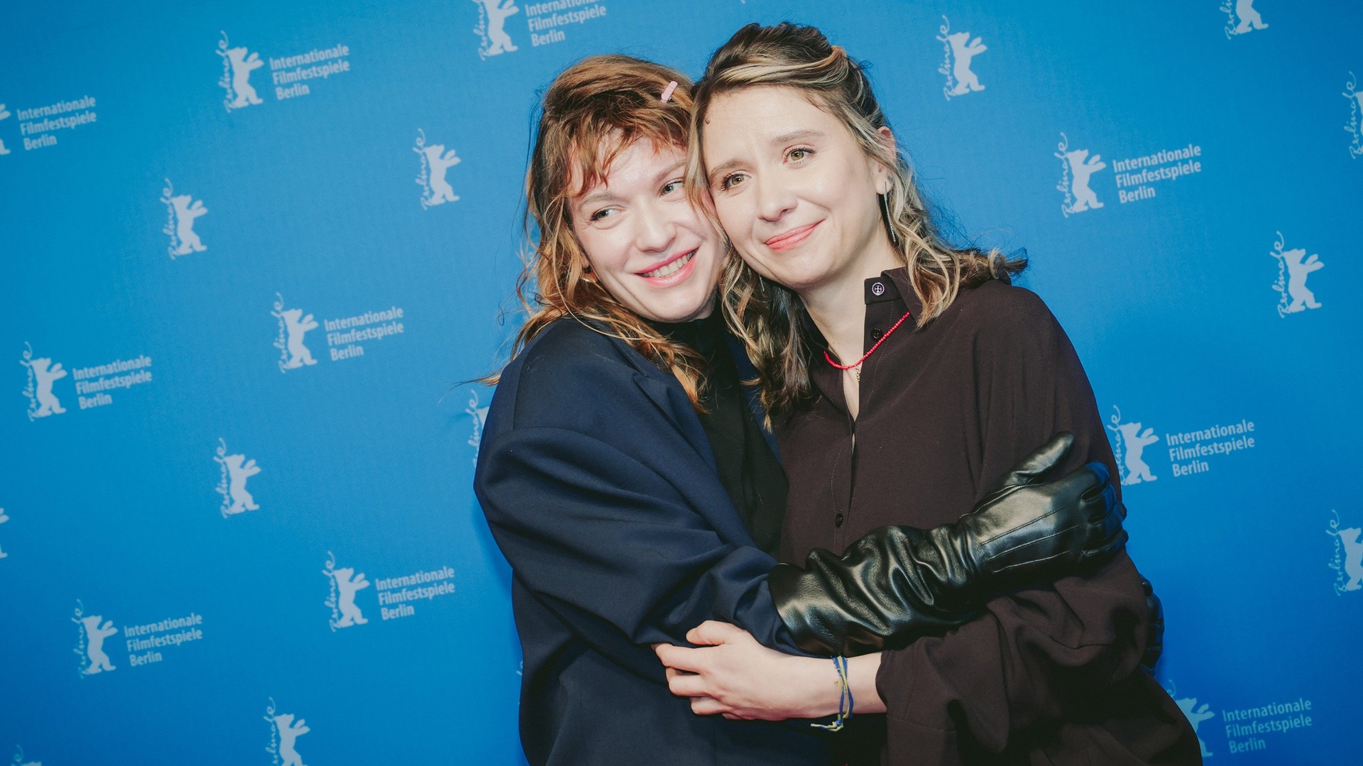 Марися Нікітюк у синьому піджаку обіймає Алісу Коваленко в чорному на синій прес-стіні Берлінале, обидві сміються
