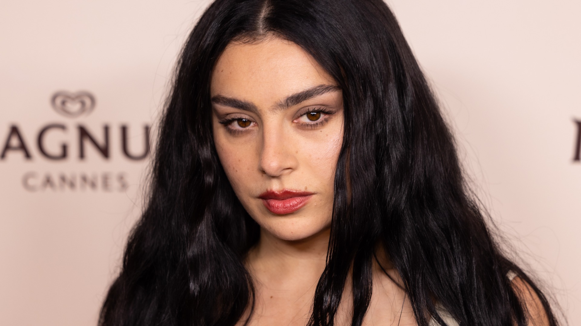 Charli XCX із розпущеним чорним волоссям і червоною помадою дивиться в камеру
