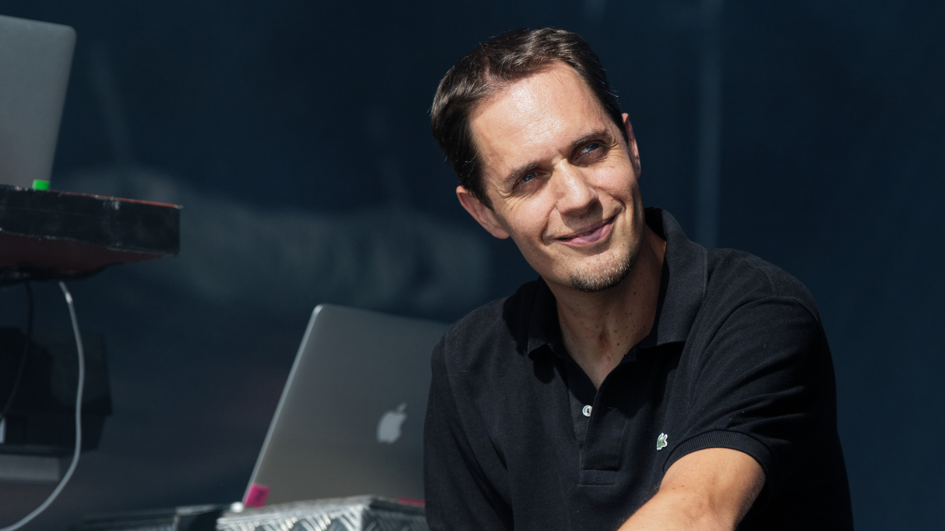 Grand Corps Malade у чорній тенісці усміхається на сцені, поруч ноутбук