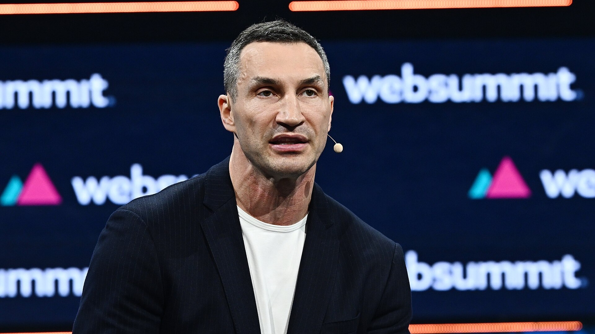 Володимир Кличко в темному піджаку й білій футболці говорить зі сцени, позаду екран із логотипами Web Summit